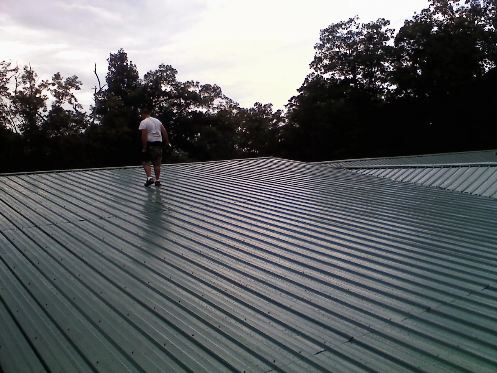 Roofer walking a wide expanse of new green metal roofing in Marana