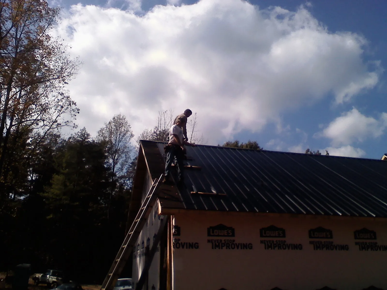 Roofer fastening dark metal panels high against a cloudy sky, from a Roof Inspection job in Marana
